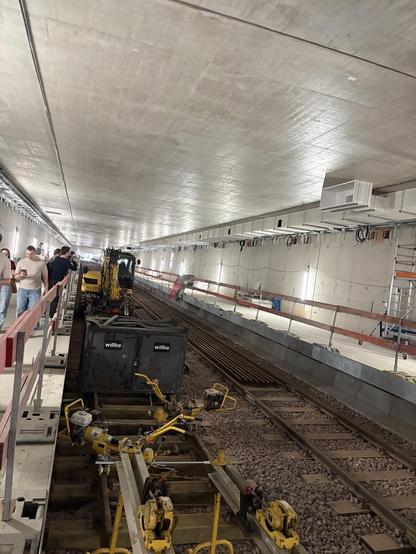 Der geschlossene Rohbau der Haltestelle Stoltenstraße mit Seitenbahnsteigen. Schotter und Gleise sind bereits verlegt und ein Arbeitszug steht auf dem linken Gleis.