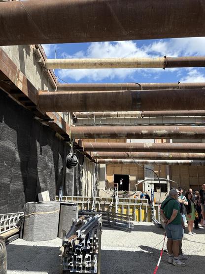 Eine offene Arbeitsgrube, die von massiven Stahlträgern seitlich abgestützt wird, es liegen Gerüstteile und Dämmmaterialen herum. Am Ende der Grube wird der Tunnel weitergeführt, die offene Flanke ist größtenteils durch Holz verschlossen.