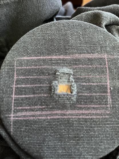 Black canvas pants have been stretched across a darning surface, showing a ragged quarter-sized hole in the fabric. There’s pink pencil marks around it in a striped flag shape showing where I will stitch the different colors.