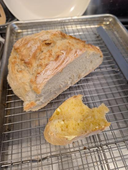 A fresh baked loaf of bread on a cooling rack, one slice cut off with butter and honey, half eaten!