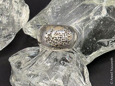 The ring is photographed among some pieces of glass. It has many deep pits in it, looking almost like lunar craters