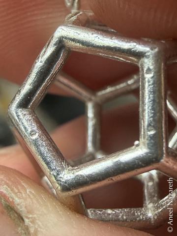 Small divots on the silver surfaces of a dodecahedron left over from the 3D Printing sprues