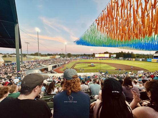 The view from the stands at a local baseball game. The skiers are blue with rose coloured clouds.