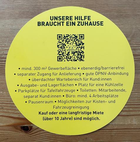 Foto eines runden gelben Flyers mit dem Text: 
UNSERE HILFE BRAUCHT EIN ZUHAUSE
- ﻿﻿mind. 300 m2 Gewerbefläche • ebenerdig/barrierefrei
- ﻿﻿separater Zugang für Anlieferung • gute ÖPNV-Anbindung
- ﻿﻿überdachter Wartebereich für Kund:innen
- ﻿﻿Ausgabe- und Lagerflächen • Platz für eine Kühlzelle
- ﻿﻿Parkplätze für Tafelfahrzeuge • Toiletten: Mitarbeitende, separat Kund:innen • Büro: mind. 4 Arbeitsplätze
- ﻿﻿Pausenraum • Möglichkeiten zur Kisten- und Fahrzeugreinigung
- Kauf oder eine langfristige Miete (über 10 Jahre) sind möglich.