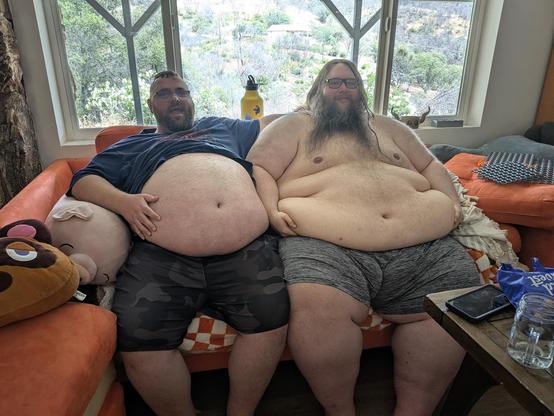 Two fat hairy caucasian dudes on an orange couch. wearin shorts, but bellies out