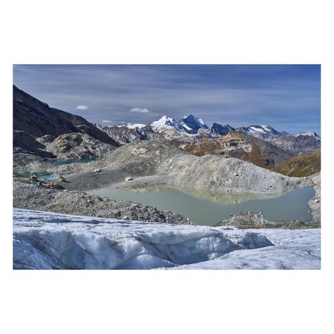 Photo d'un paysage de haute montagne.
Au tout premier plan, on voit le front d'un glacier qui descend vers un groupe de petits lacs aux eaux laiteuses en contrebas. Les reliefs, caillouteux, laissent penser que le retrait du glacier est très récent. 
Au fond, l'horizon est fermé par de hautes montagnes enneigées. Le ciel est légèrement voilé.
-
A photo of a high-mountain landscape.
In the very foreground, you can see the front of a glacier descending toward a group of small lakes with milky-white water below. The rocky terrain suggests that the glacier’s retreat is very recent.
In the background, the horizon is framed by tall, snow-capped mountains. The sky is slightly overcast.