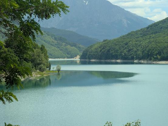 Photo d'un lac de montagne (lac du Sautet). Sur les bords et en arrière plan, des montagnes verdoyantes, et sur celle du fond des rochers encore un peu enneigés.

Sur la gauche de la photo, une petite pointe au bout de laquelle se tient un petit arbre. La pointe semble se poursuivre dans l'eau sous la forme d'une zone de pétole (eau lisse, absence de vent) que la risée contourne soigneusement.
