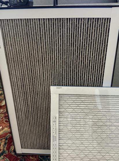 Air filter box with used filter, quite dark, next to fresh new white filter