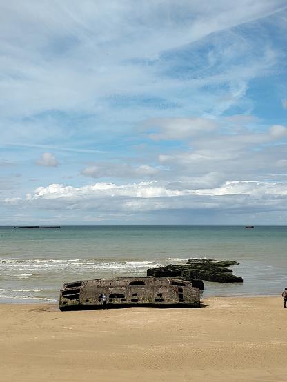 Das Bild Zeit verwitterte Ponton Brückenelemente die teilweise am Strand und teilweise  im Meer liegen. Sie liegen am Gold Beach in Arromanches in der Normandie und stammen von der Landung der Alliierten im Juni 1944