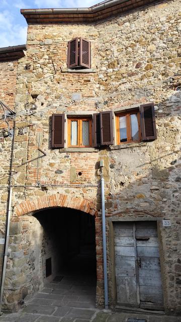 Steinfassade mit Torbogen und Holztür.
im 1. OG zwei Fenster mit Läden.
ganz oben eines mit geschlossenen Fensterläden