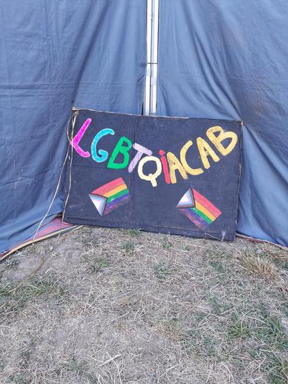 Un panneau artisanal orné de deux drapeaux des fiertés. On peut y lire "LGBTQIACAB"