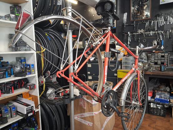 Un vieux vélo motobecane orange dans un atelier vélo. Suspendu à un pied d'atelier, la roue arrière retirée.