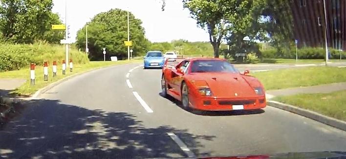 A red Ferrari F50 driving on a road with other cars and trees in the background.