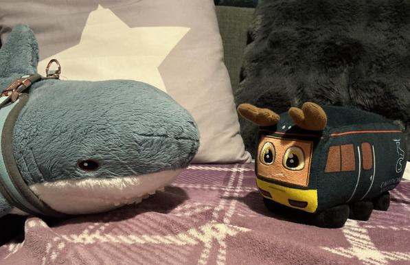 A Blåhaj cuddly shark and a cuddly train with antlers and in a Caledonian Sleeper livery talking to each other.