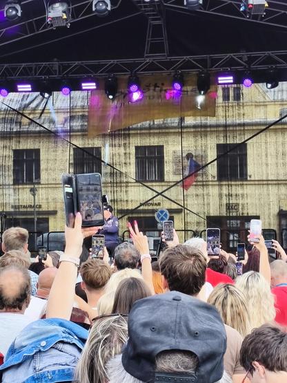 Koncert, pohled z publika na jeviště, které stíní mobily. Lidé si na ně natáčí umělce.