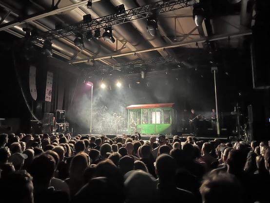 Shot of a stage with a hut in the middle, taken from way back among the audiencd