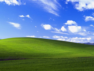 The Bliss image used for the Desktop in Windows XP. It shows a blue sky with a few puffy white clouds, and a rolling hillside with patches of sunshine highlighting parts.