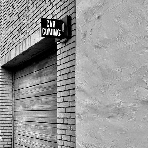 Black and white photo of the exit to a parking garage with a sign that says Car Coming but the top of the O is somewhat missing so it looks kind of reads like Car Cumming if you're only half paying attention.