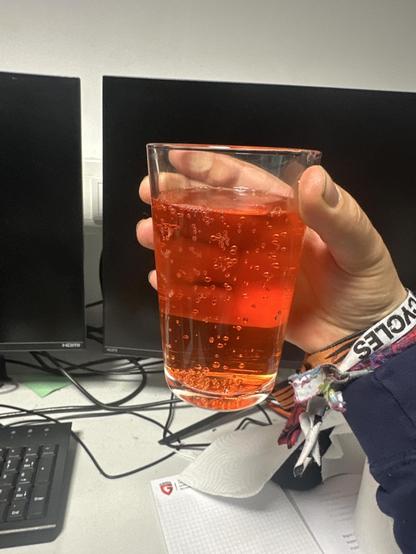 Bild von einem normalen Getränkeglass welches eine Flüssigkeit enthält, die wie Aperol Spritz aussieht, also Orange-Rot und durchsichtig.