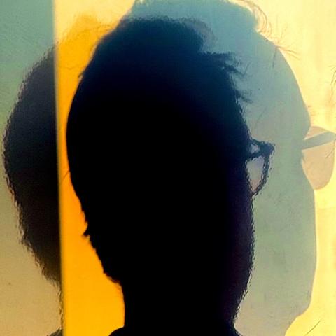 Shadows of a bespectacled man's head on a wall.