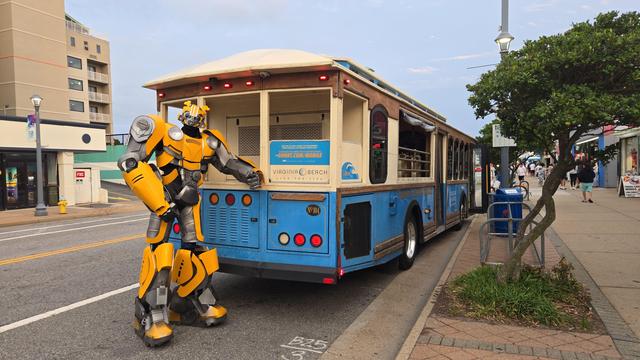 a street performer dressed in an elaborate costume depicting the character 'bumblebee' from the 'transformers' franchise posing next to my beach trolley.