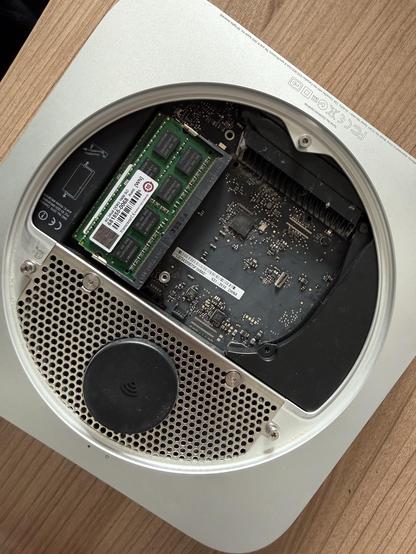 Ein offenes Computergehäuse mit den internen Komponenten, einschließlich RAM-Modulen, einer Leiterplatte und einem Lüfter. Der Hintergrund zeigt eine Holzoberfläche.