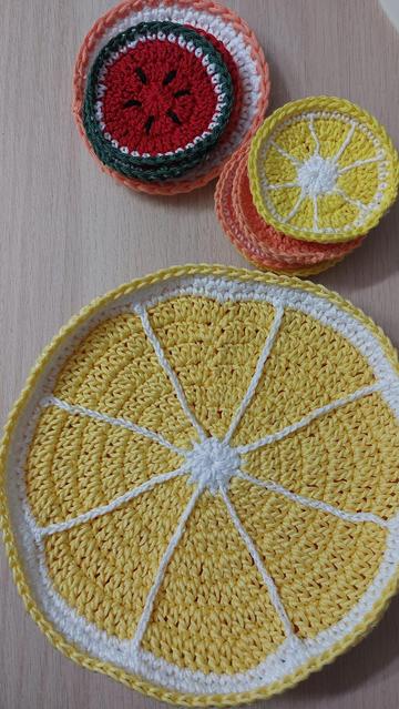 Crochet circles of various sizes and colours laid out on a wooden surface. You can see watermelon, lemon, and orange slices.