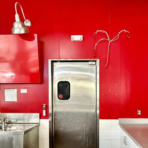 Stainless steel door against a red wall in a vacant mall food court. White electrical lines are coming out of the wall implying that more used to be there.