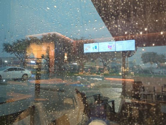 An image of a very rainy window with the reflection of the interior of a coffee shop chain