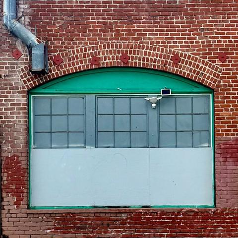 Window on the side of a brick building. The lower half is covered with a white panel and the upper section is under an arch and painted mint green.