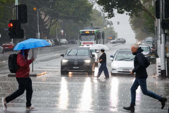 a photo from The Age of a rainy Melbourne streetscape.  Pedestrians are apparently hurrying across the road, there are a few cars in the middle-ground and some trams in the background