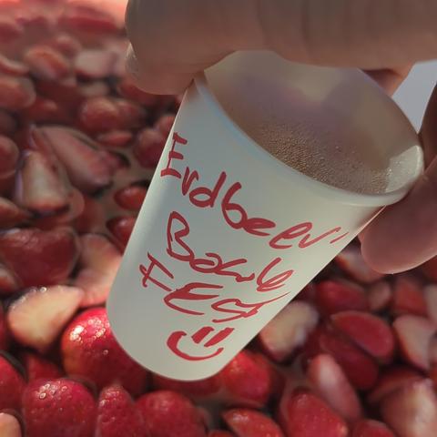 Becher wird über Eimer mit Erdbeerbowle gehalten. "Erdbeerbowlefest :-)" ist auf Pappvecher gekritzelt.