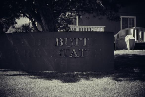 A severely worn sign for a housing complex that now reads “BUTT TAT.” Faint outlines reveal that it once held enough letters to read “PILOT BUTTE PARK ESTATES.”