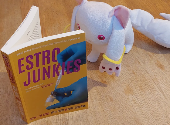 Kyubey (A white cat-ish alien from the anime Puella Magi Madoka Magica) reading a paperback copy of Estro Junkies