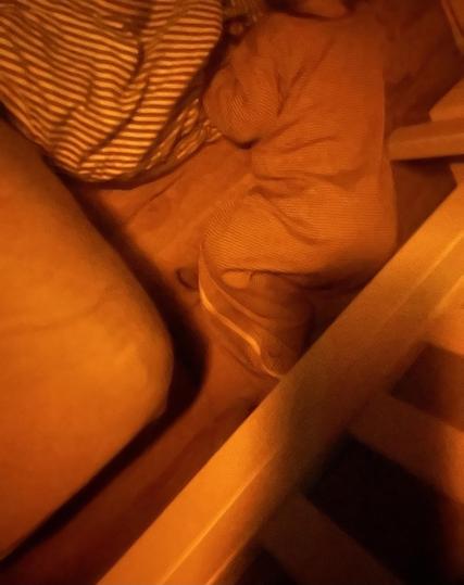 Unscharfes Bild von einem Baby im Schlafsack, das auf dem Boden neben einer Matratze liegt. Das Gesicht des Babys ist nicht zu sehen. Neben dem Baby liegt ein gestreiftes Kopfkissen.