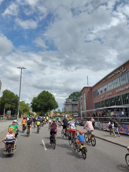 A convoy of bikes cycling through Hamburg Sternschanze, with the Flakbunker in the background.