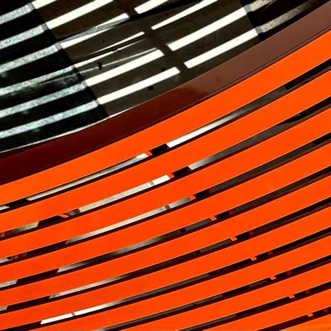 Orange metal slatted bench casting some shadows