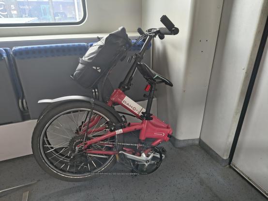 Ein rotes Faltrad lehnt an Klappsitzen in einem Zug.
