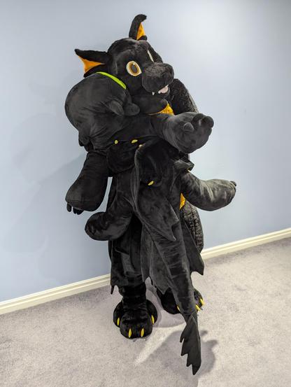 Black and copper dragon fursuit clutching a plushie toothless that's almost as big as him