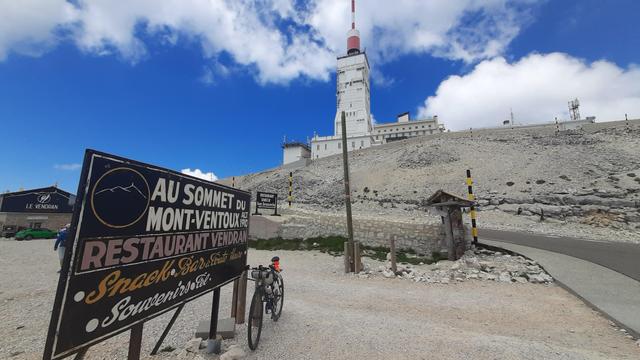 The semaphore tower on Mont Ventoux  against a postcardbloäue Skype. A bit of the stony summit. My bike leaning against a billboard advertising a restaurant