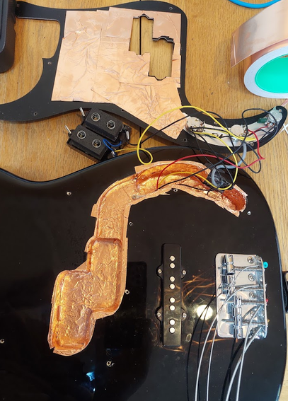 A bass guitar's body which has been opened up. The cavity and underside of the pickguard have been covered with copper tape.
