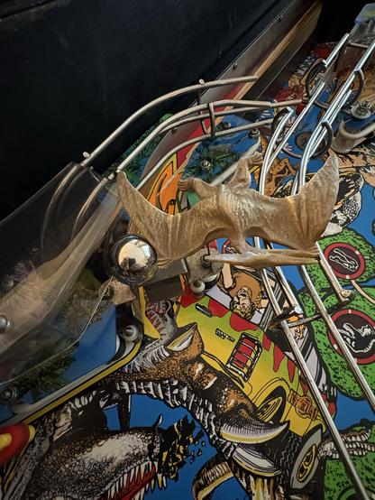 Middle playfield of a Data East Jurassic Park (1993) pinball machine. A pinball is sitting on top of the shooter lane gate, stuck between a Pteranodon miniature and a transparent plastic protector (which is supposed to prevent the being being stuck elsewhere, lol)