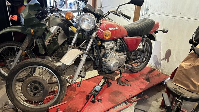 A red 1979 Kawasaki KZ400 motorcycle that is sitting on a motorcycle lift. It is in pretty beat up condition.