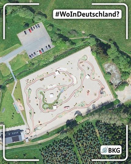 Luftbild einer großflächigen Anlage mit verschlungenen, hellen Wegen. Die Anlage liegt in einer grünen Umgebung mit Bäumen, Wiesen und einem Parkplatz. Über dem Bild steht die Frage „#WoInDeutschland?“, unten rechts ist das BKG-Logo eingeblendet.