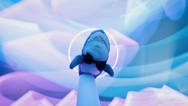 Smolhaj (small IKEA shark) with a bow tie under a white light halo surrounded by cyan and pink light streaks