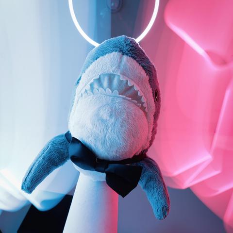 Smolhaj (small IKEA shark) with a bow tie under a white light halo surrounded by cyan and pink light streaks