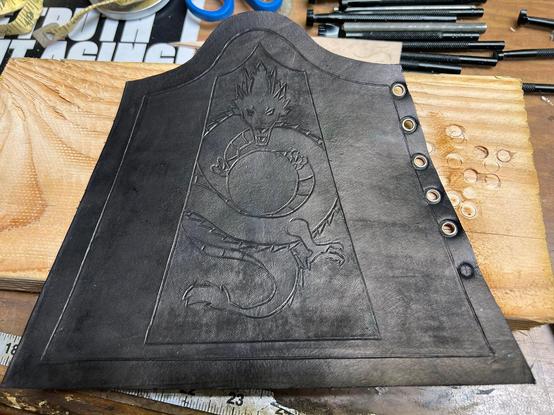Leather vambrace work in progress with embossed design, now with several holes punched and grommets placed, and it has been dyed a basic black.