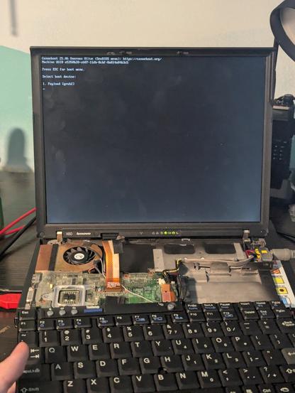 A x60 with its internals spread apart. Tools litter its sidelines. On the dim screen is the boot prompt