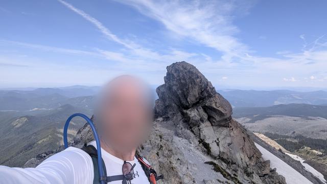 A man with a blurred face on a rocky Ridgeline with patches of snow. A wide expanse in the background