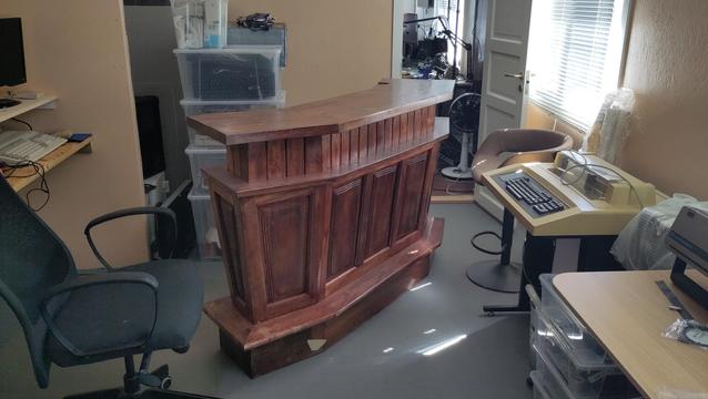 A small brown wooden corner bar in the middle of a room filled with 40 to 50 year old computers.
